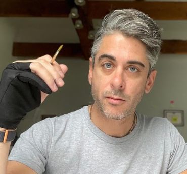 A hand reaching for paint tube in art studio with brushes and canvas frame.